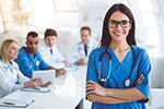 Smiling nurse wearing medical attire and stethoscope with medical professionals sitting in the background